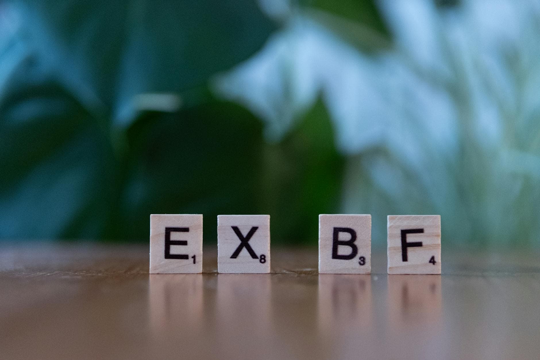 Close-up of Scrabble tiles spelling 'EXBF' on a wooden table with blurred background.