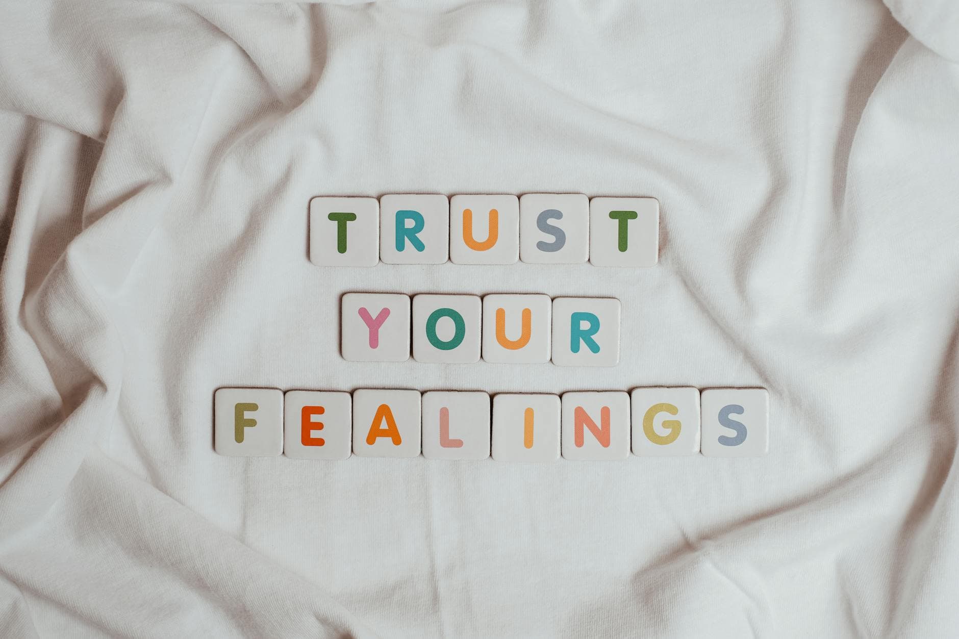 Colorful tiles spell out 'Trust your feelings' on a fabric background.