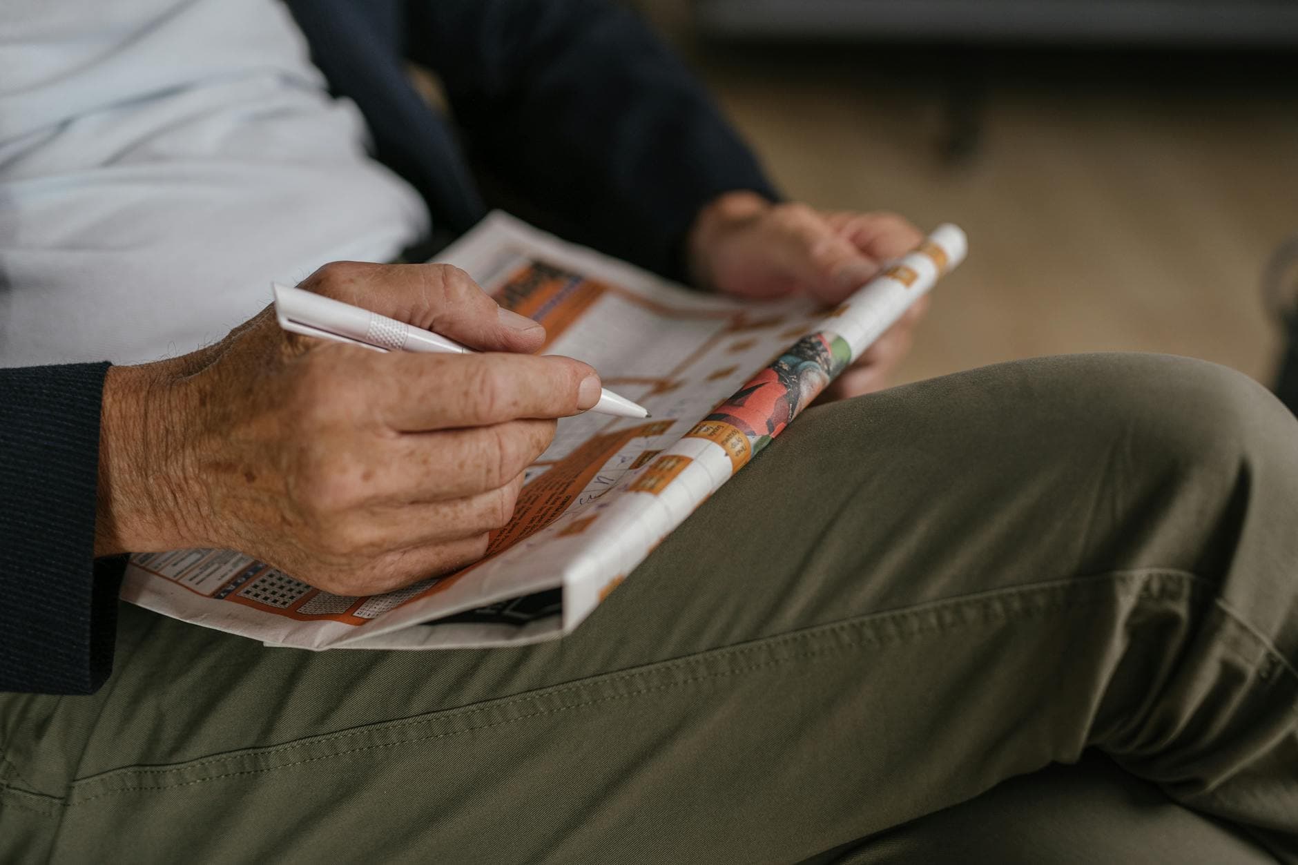Close-up of a senior adult solving a crossword puzzle in a newspaper with a pen.