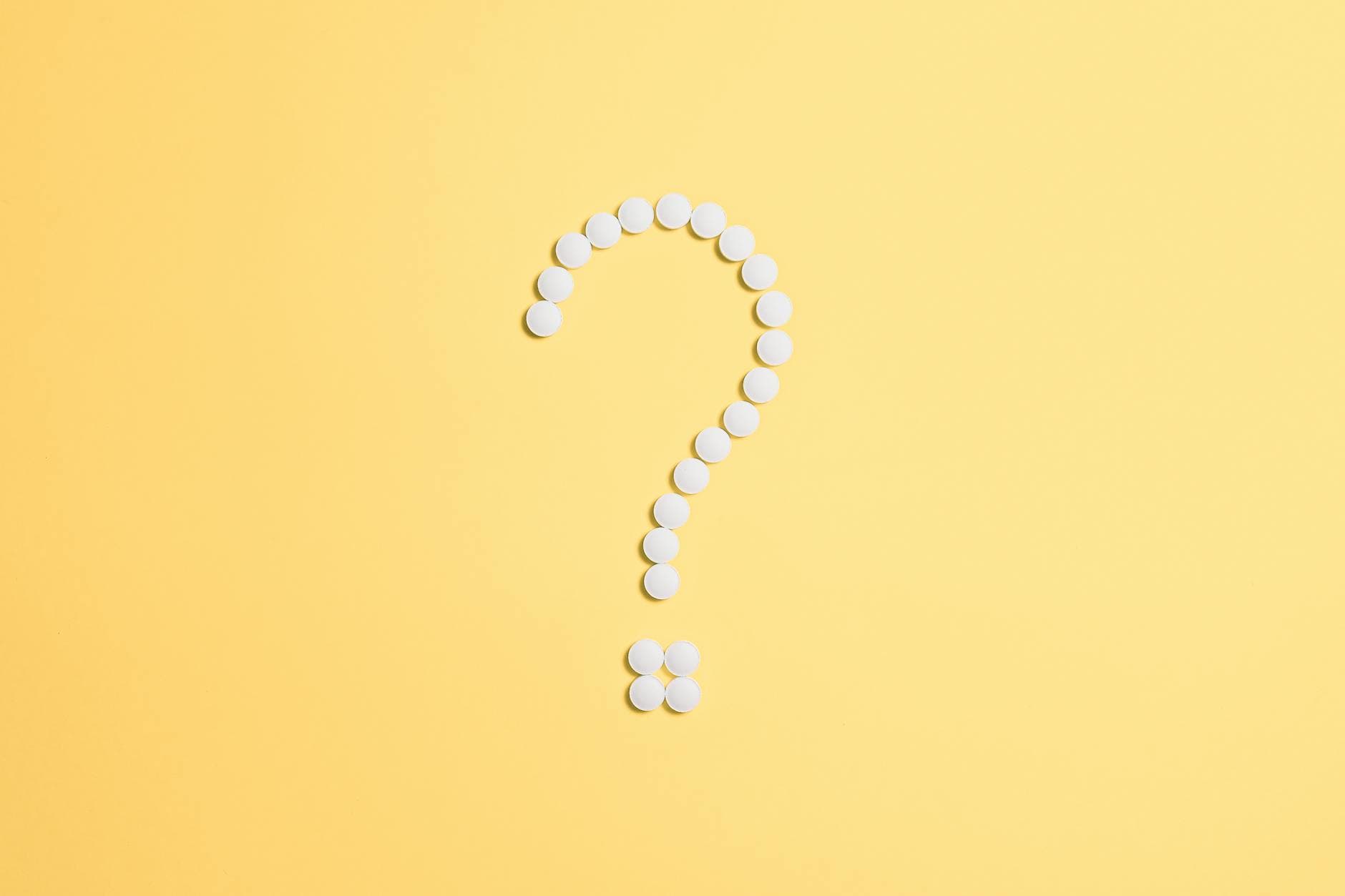 White pills arranged into a question mark shape on a vibrant yellow background.