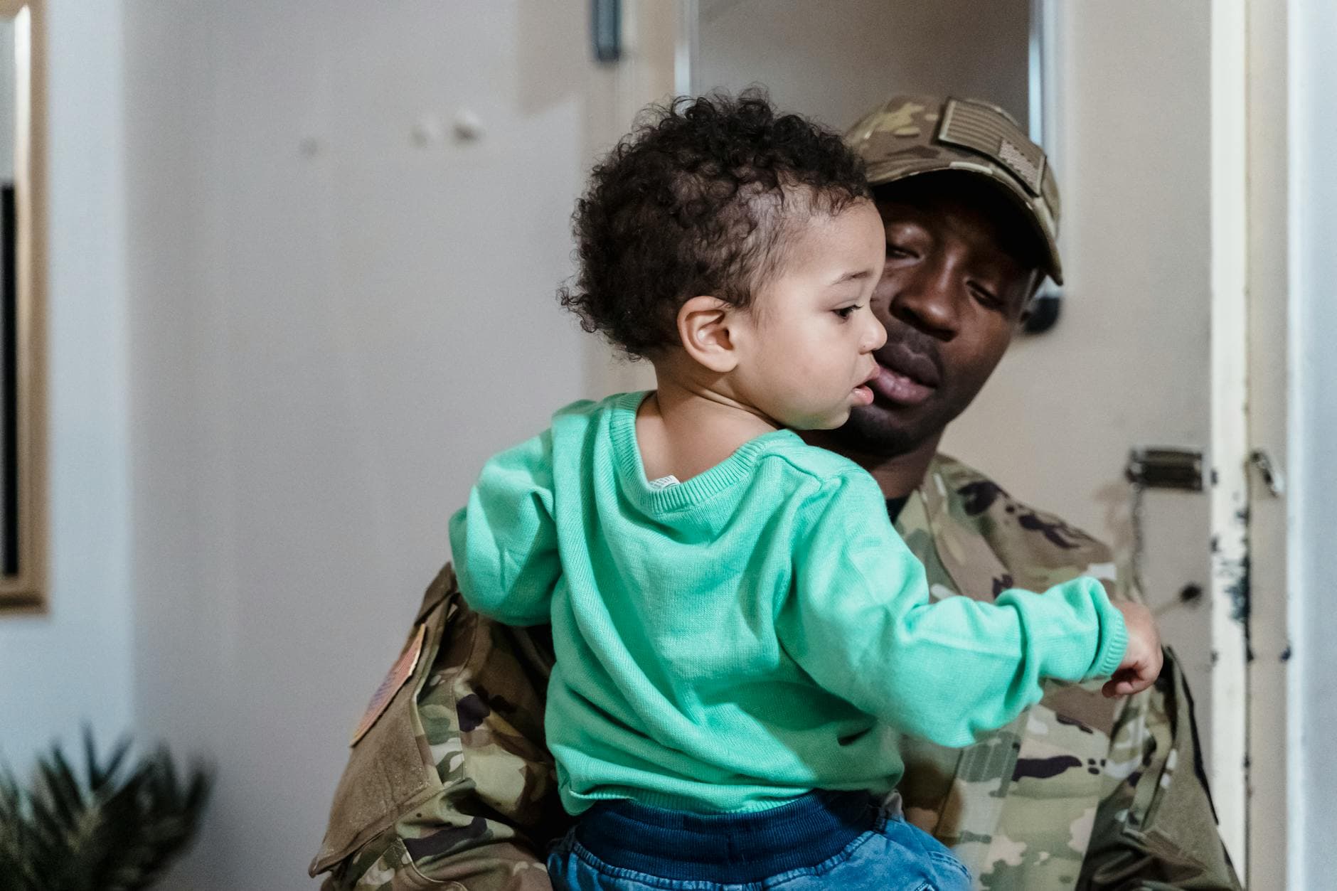 Military father in uniform lovingly holding his young child indoors.