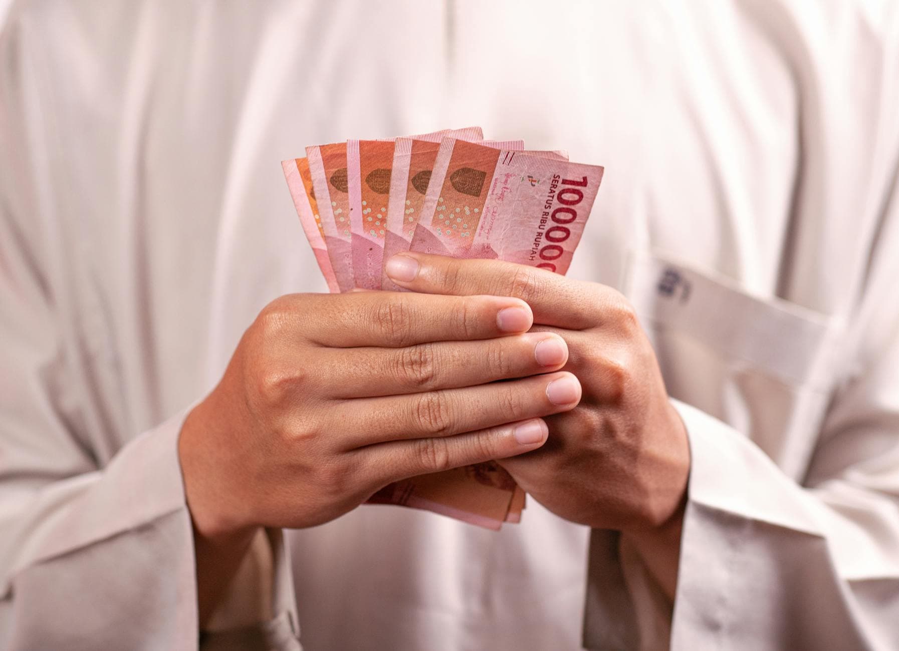 Close-up of hands holding 100,000 Indonesian Rupiah notes, symbolizing wealth and finance.