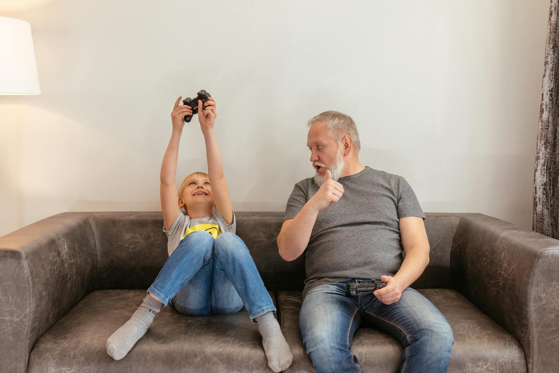 A grandfather and grandson share fun moments playing video games on a sofa.