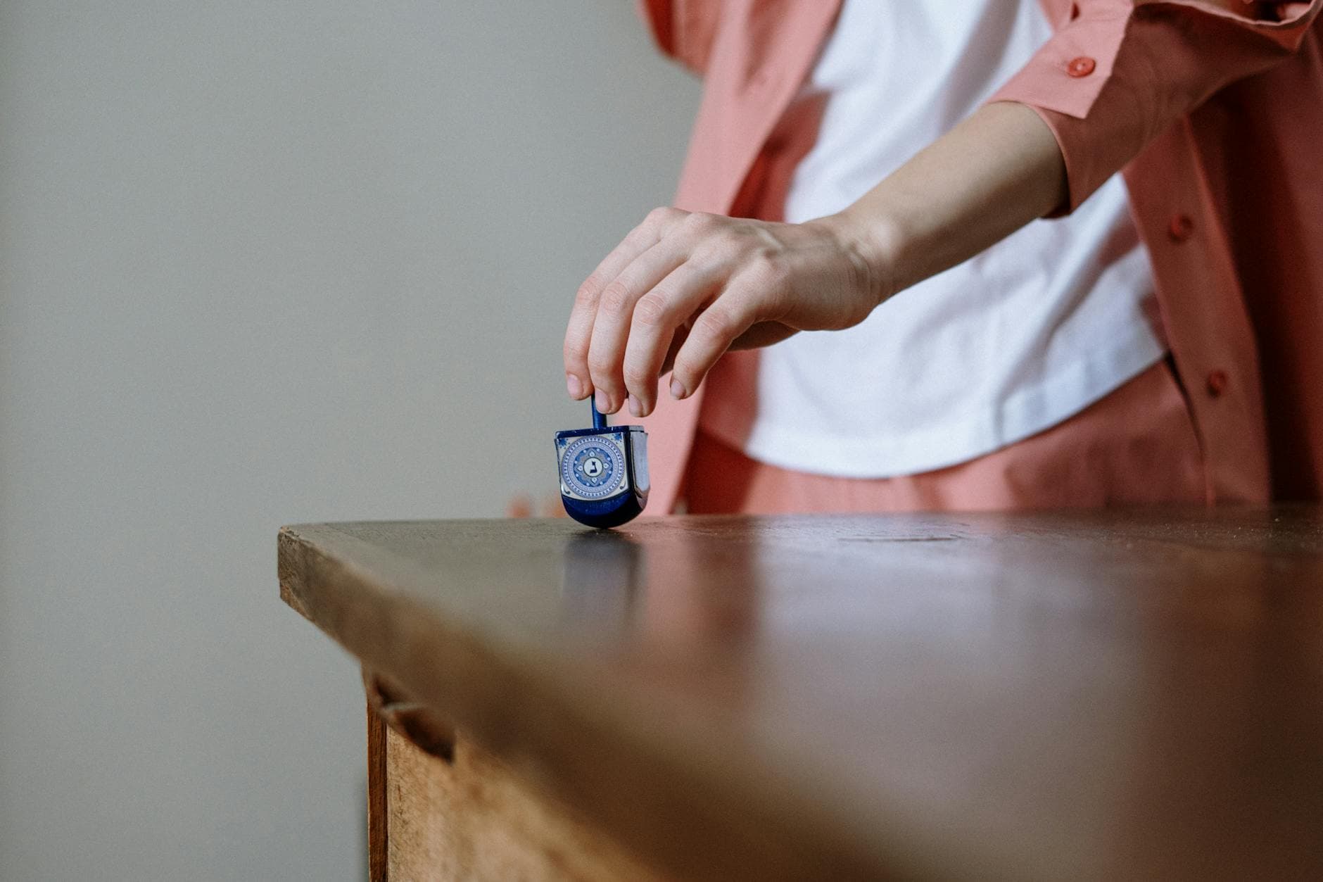 A hand spins a blue dreidel on a wooden table, symbolizing Hanukkah traditions.