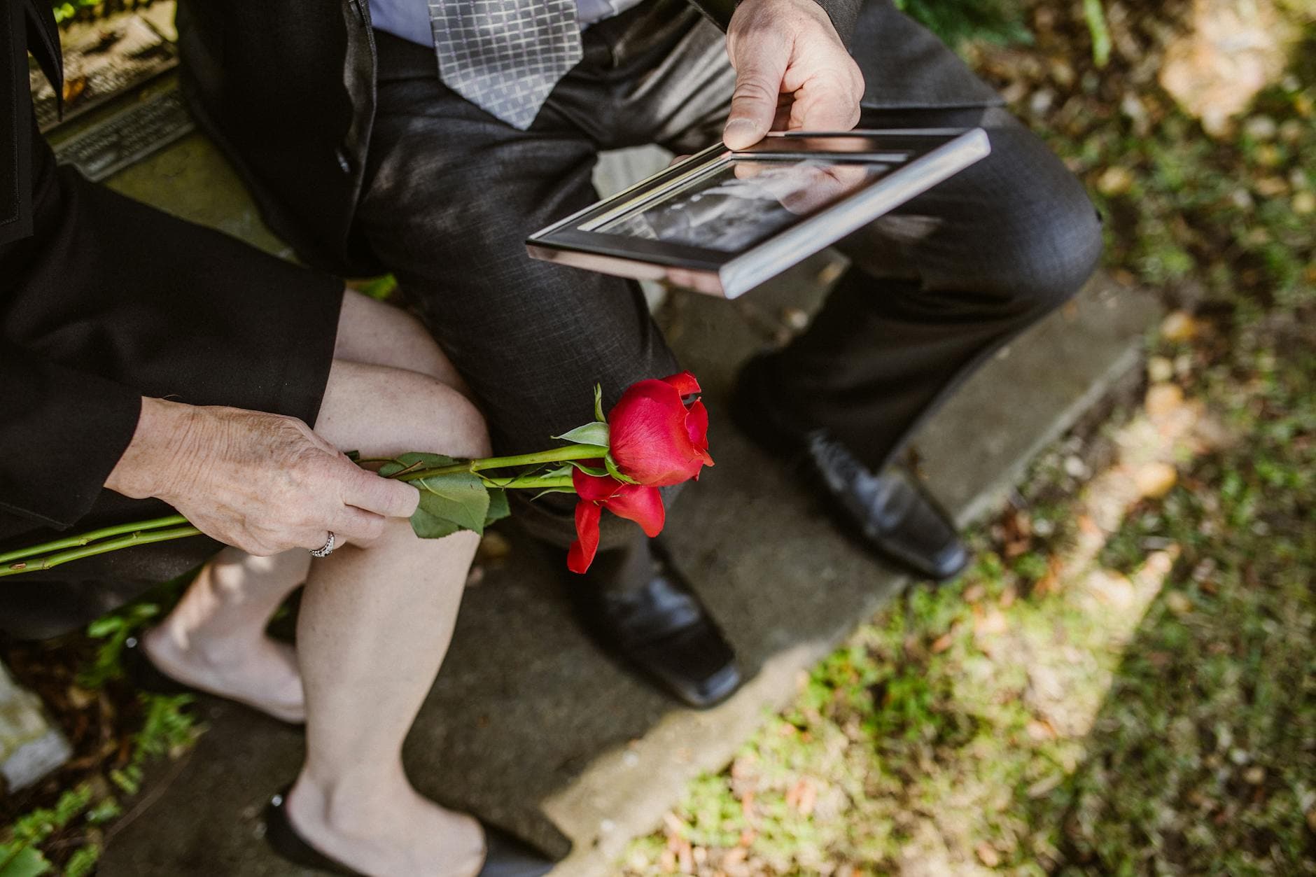 A grieving couple sitting with a red rose and a picture frame in their hands.