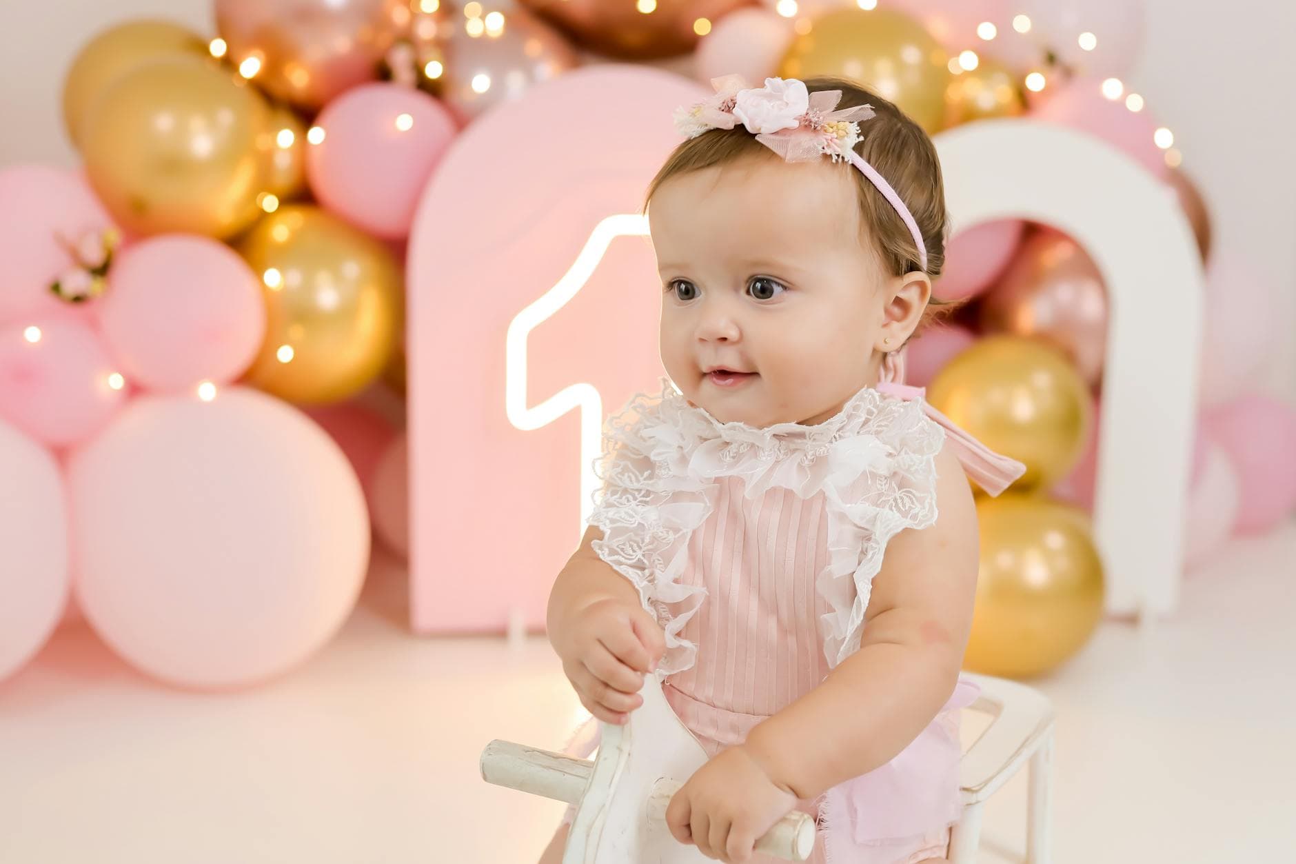 Cute baby girl during a colorful first birthday celebration with balloons.