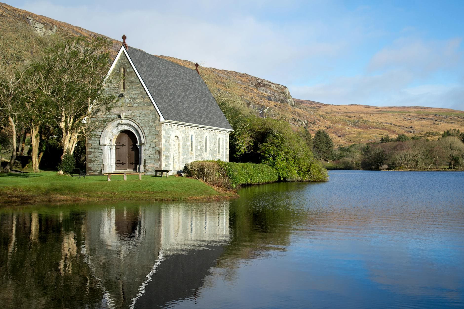 Tranquil scene of St. Finbarr's Oratory reflecting on a serene lake in Ireland with rolling hills.