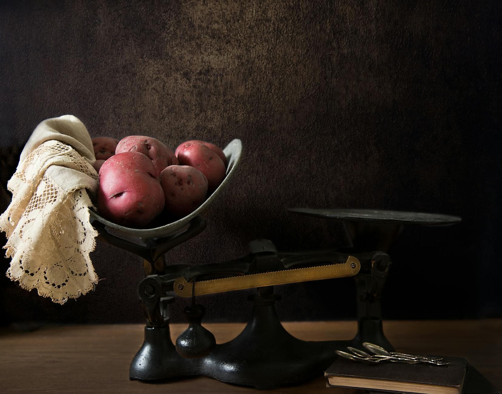 Vintage balance scale with red potatoes and lace cloth, evoking a nostalgic rustic feel.