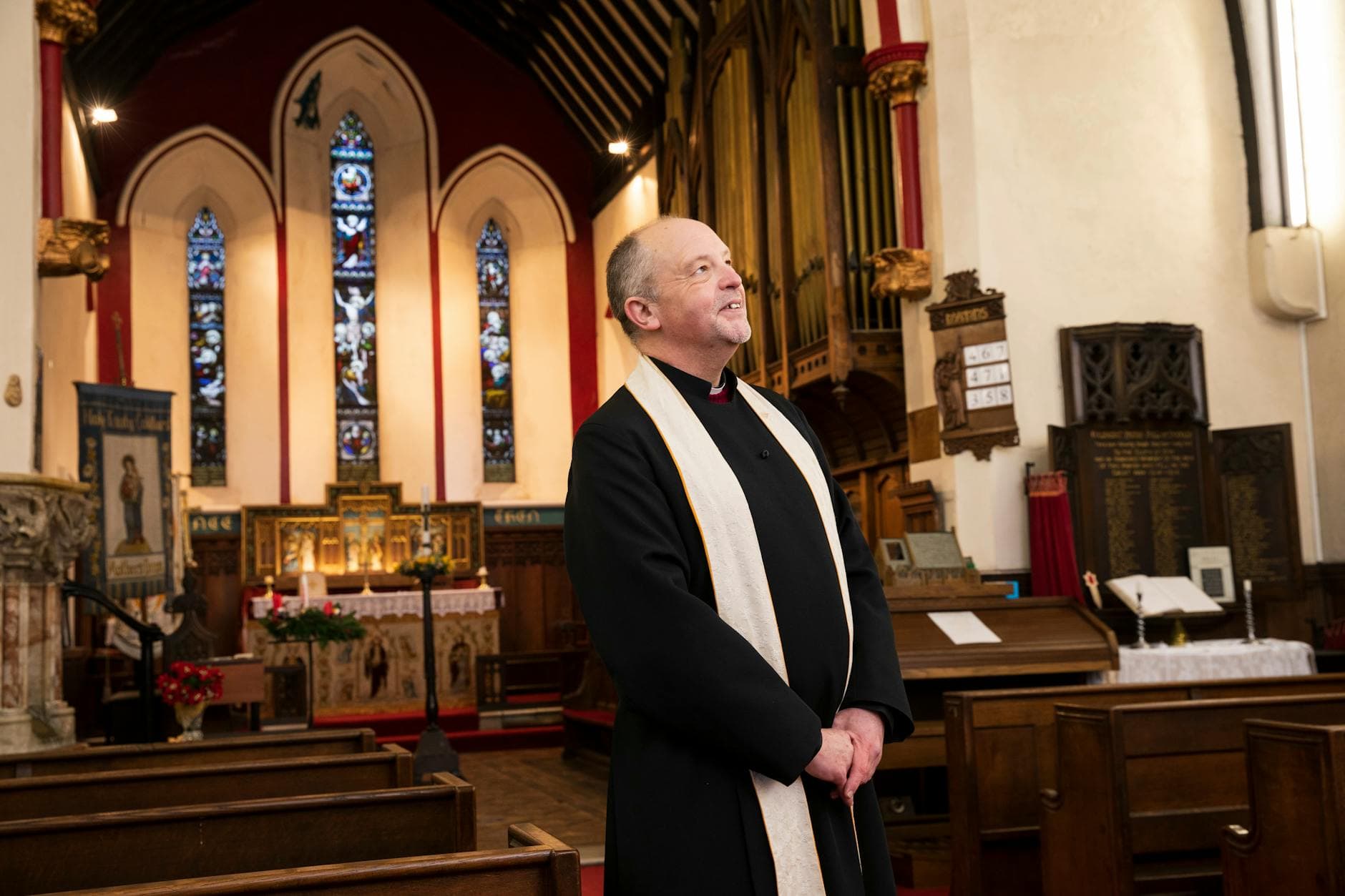 A clergyman smiling inside a beautifully decorated church, standing near the altar.