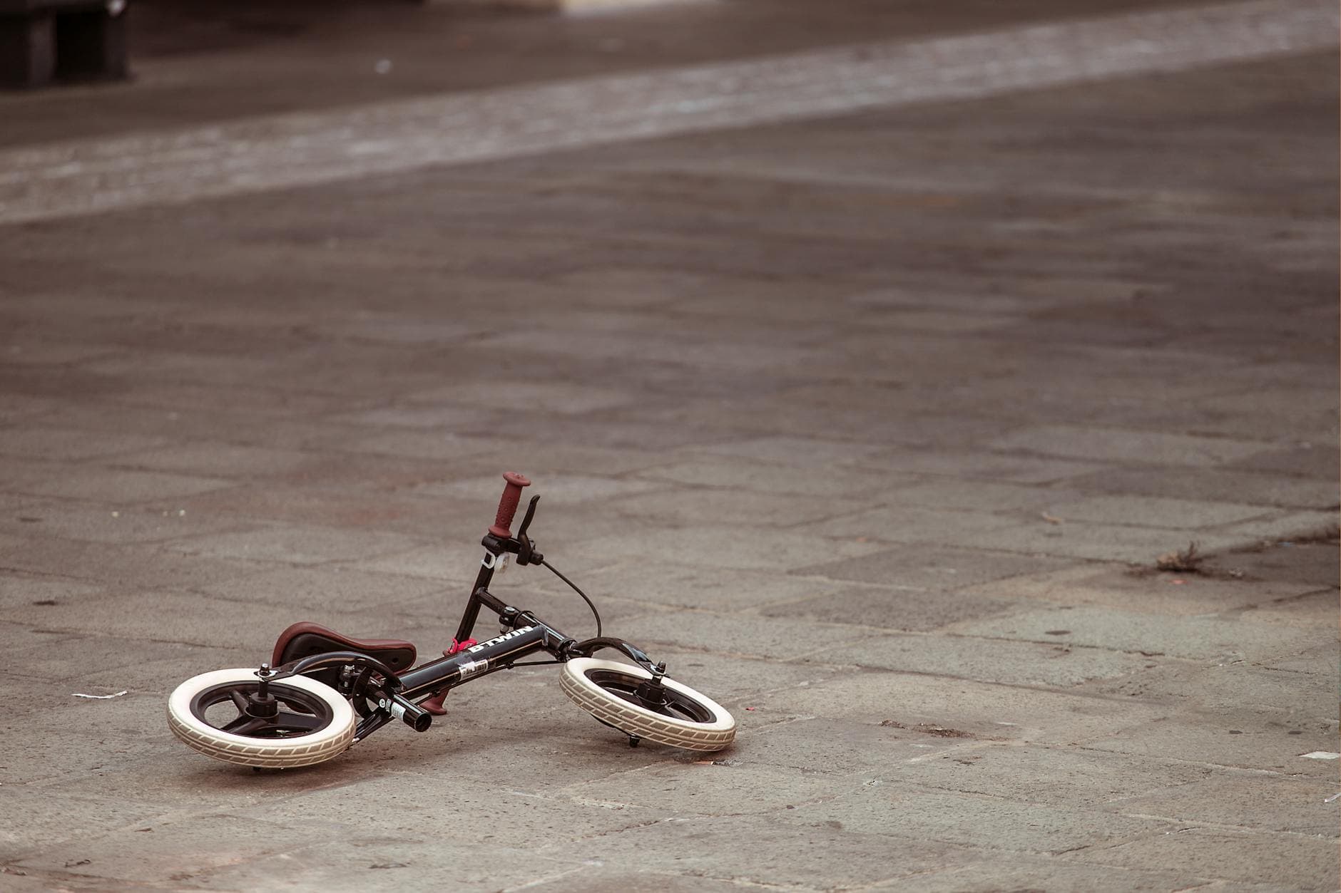 A small child's bike lies on an empty cobblestone street, evoking a sense of mystery and solitude.