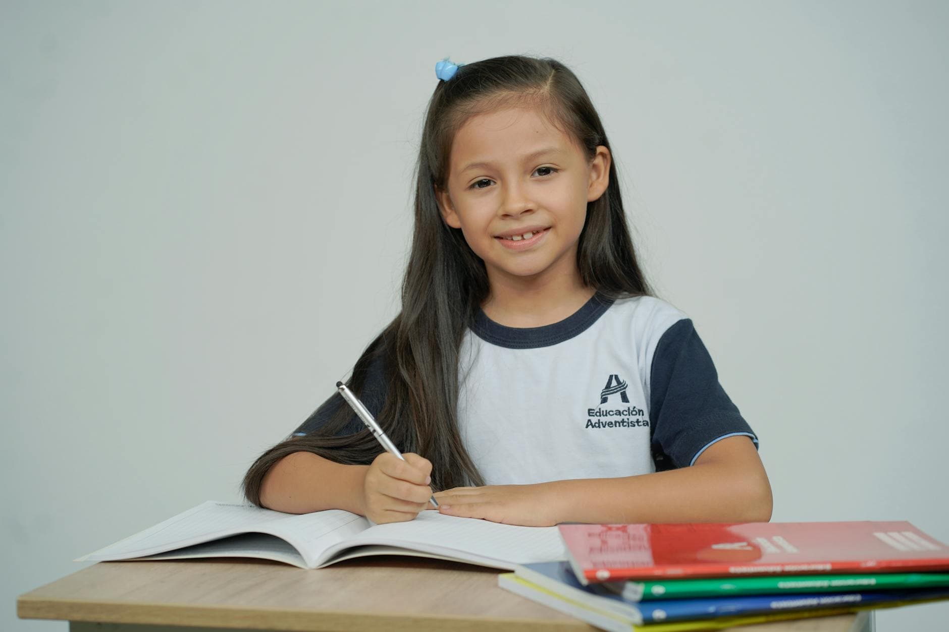 A young girl sitting at a desk, studying with open books and smiling.