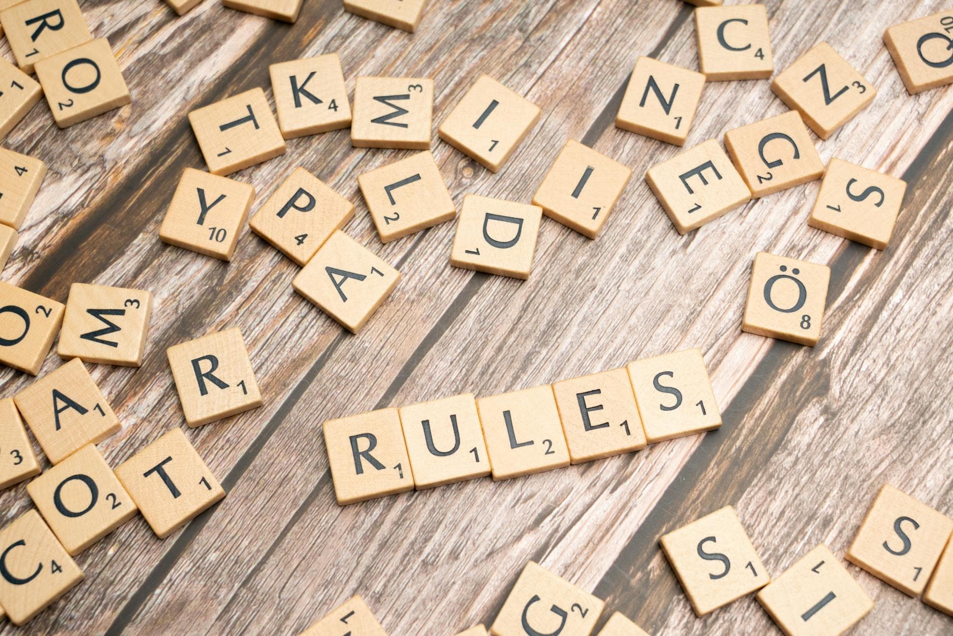 Wooden letter tiles arranged to spell 'Rules' on a textured wooden background.