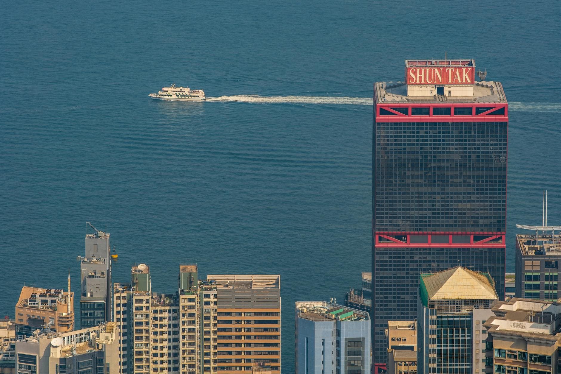 Aerial view of Hong Kong's harbor featuring high-rises and a ferry cruise.