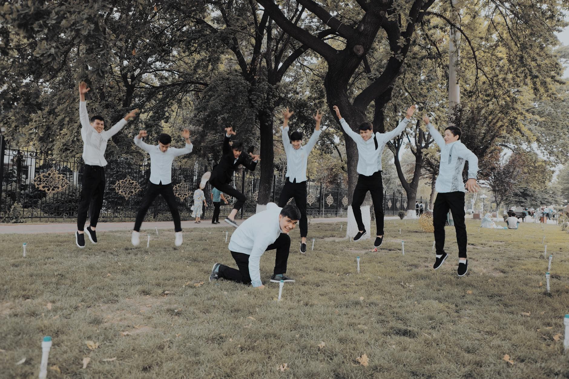 Cheerful group of young men jumping and having fun outdoors in a green park.