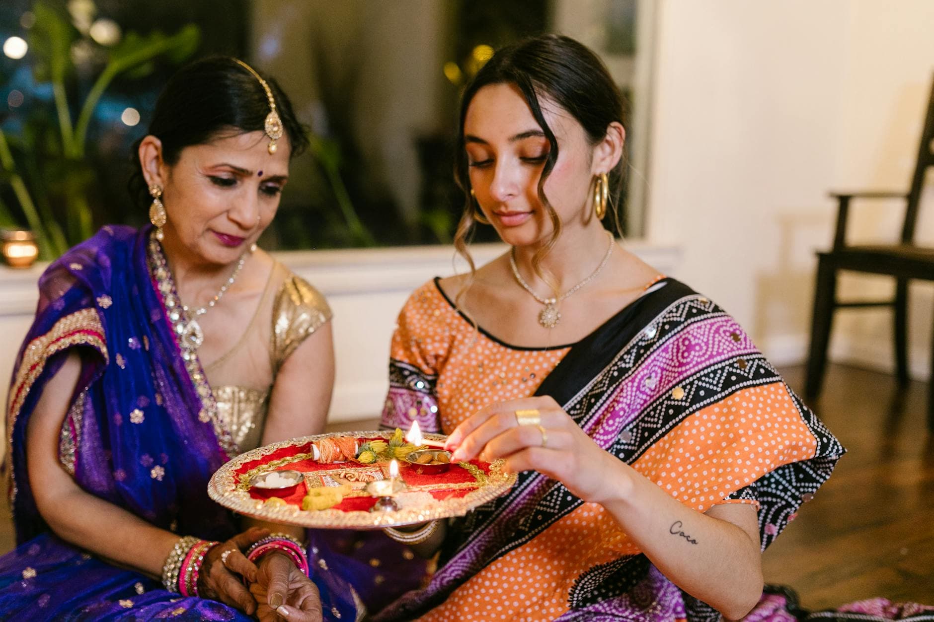 Mother and daughter performing a Diwali ritual with a lit puja plate, showcasing traditional Indian culture.