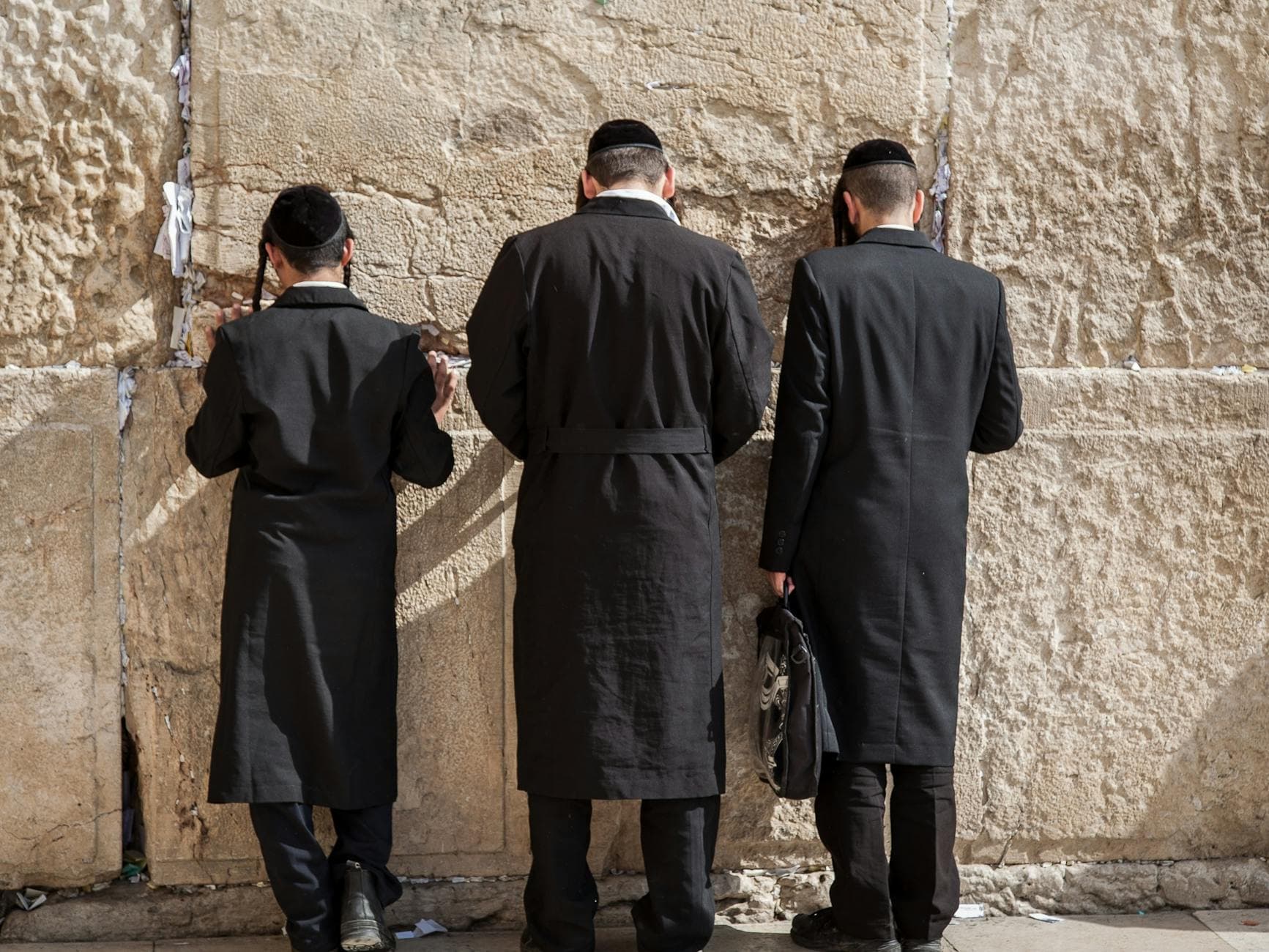Orthodox Jewish men facing the Western Wall in Jerusalem, deep in prayer and contemplation.