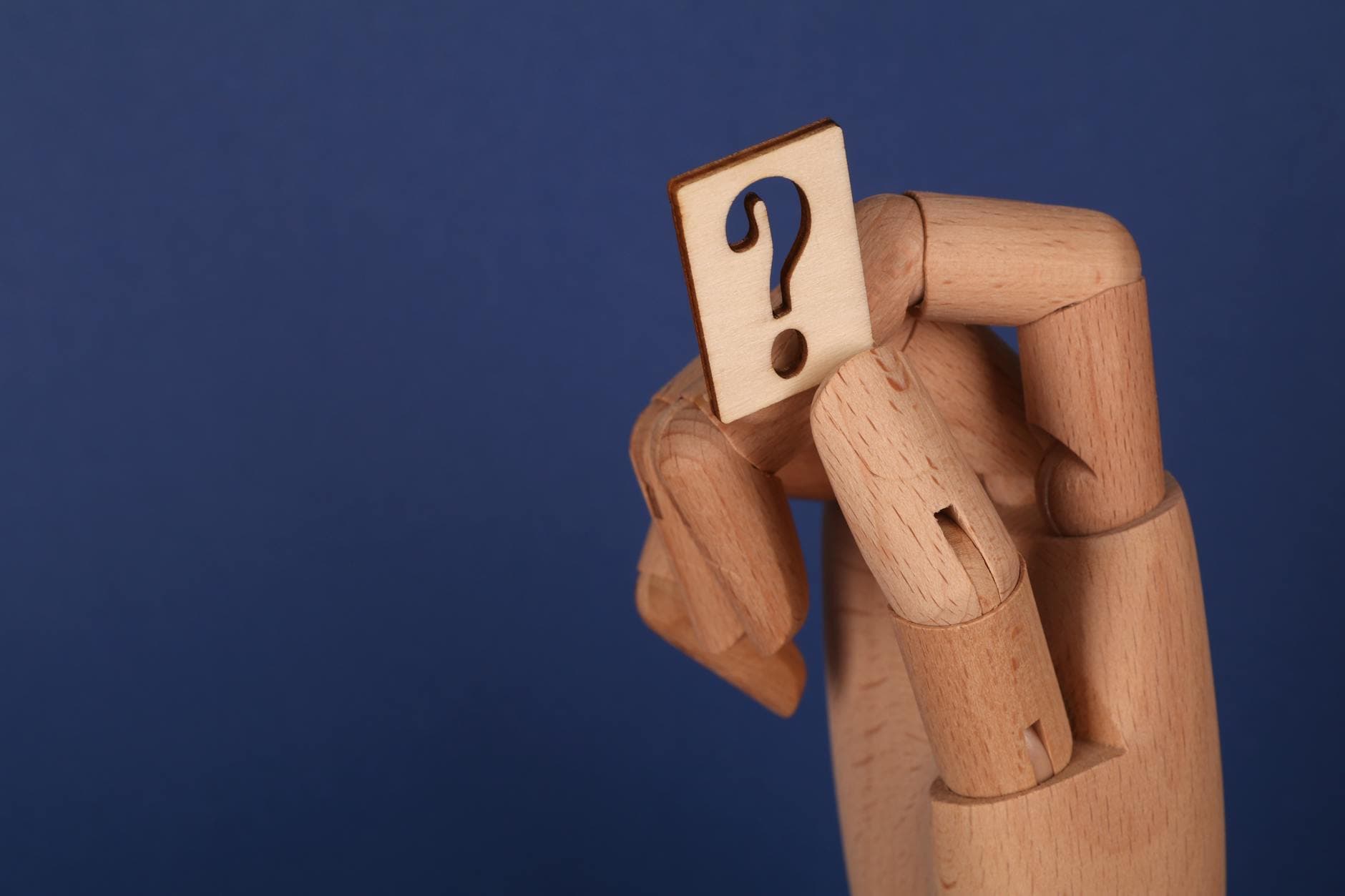 A symbolic wooden hand holding a question mark block against a blue background, representing curiosity and inquiry.