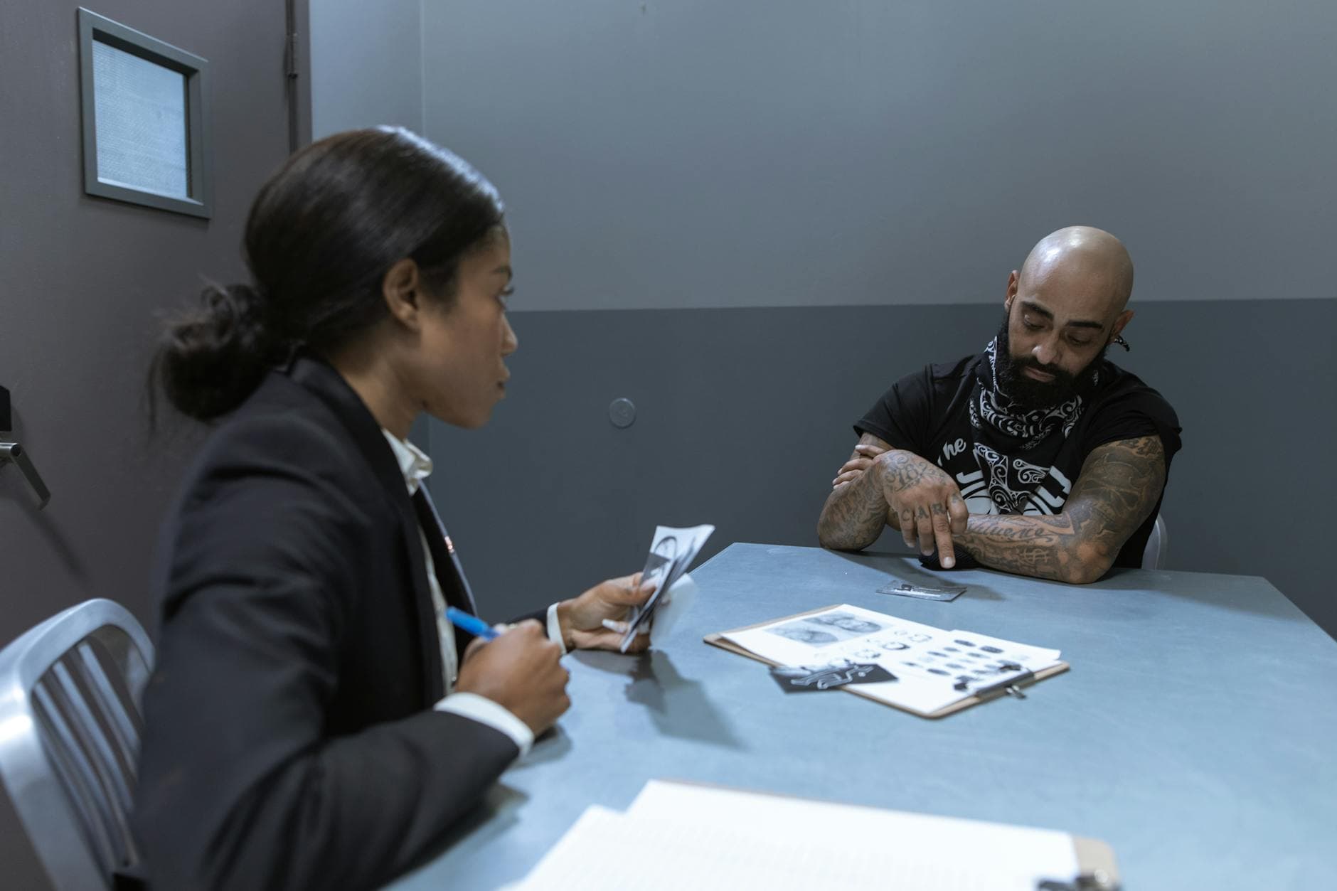 Police officer interrogating a suspect in an investigation room with documents and evidence on the table.