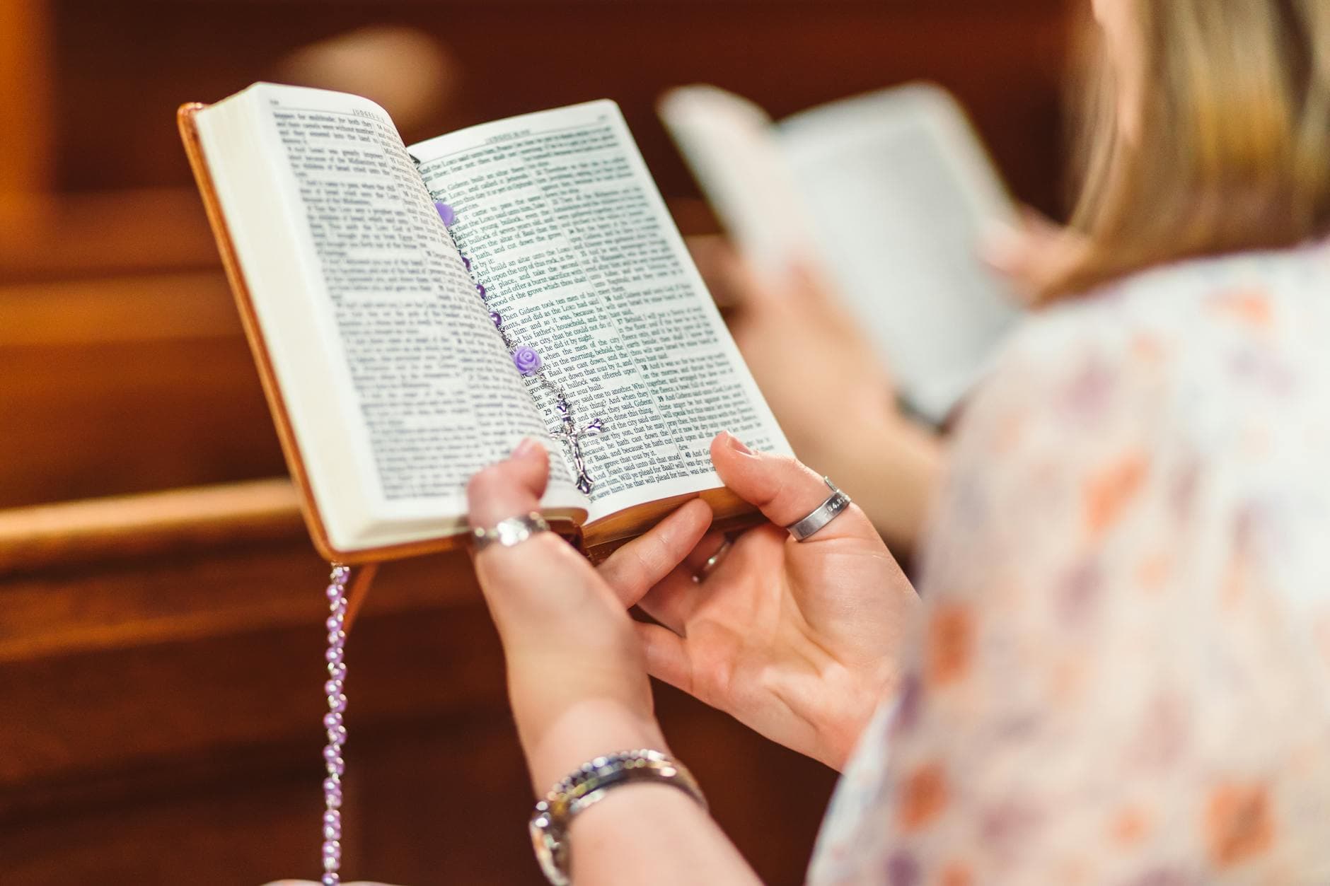 A woman holding a Bible and rosary beads, engaged in prayer inside a church.