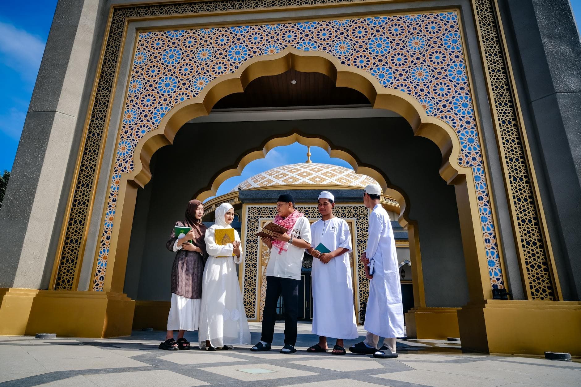 Diverse group of young Muslims discussing and learning outside a mosque entrance.